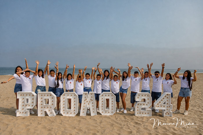 Promoción escolar celebrando junto a las letras PROMO 24 en la playa